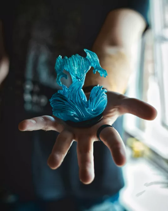 Photograph of a blue gaming desk toy sitting in Alex's palm.